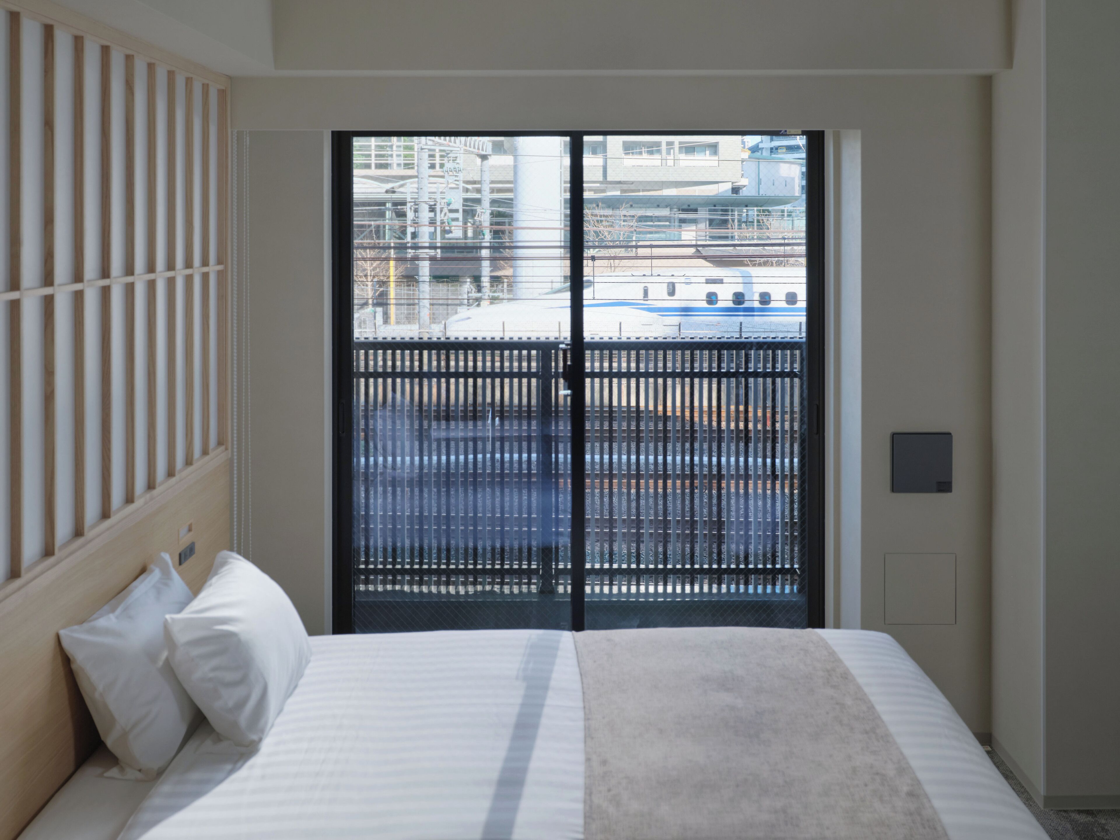 Hotellihuone, jossa on sänky, ikkuna, josta avautuu näkymä teollisuusalueelle, ja seinään kiinnitetty termostaatti.