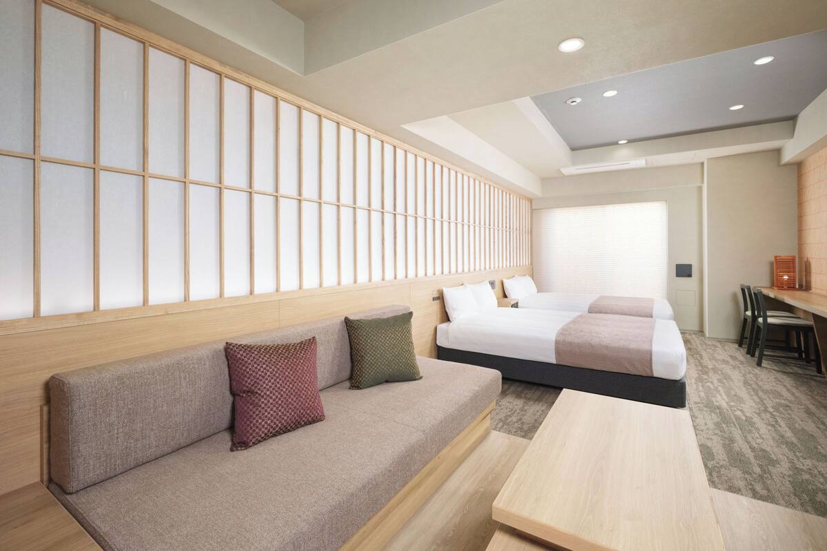 Habitación de hotel con sofá, dos camas, escritorio y vista al exterior.