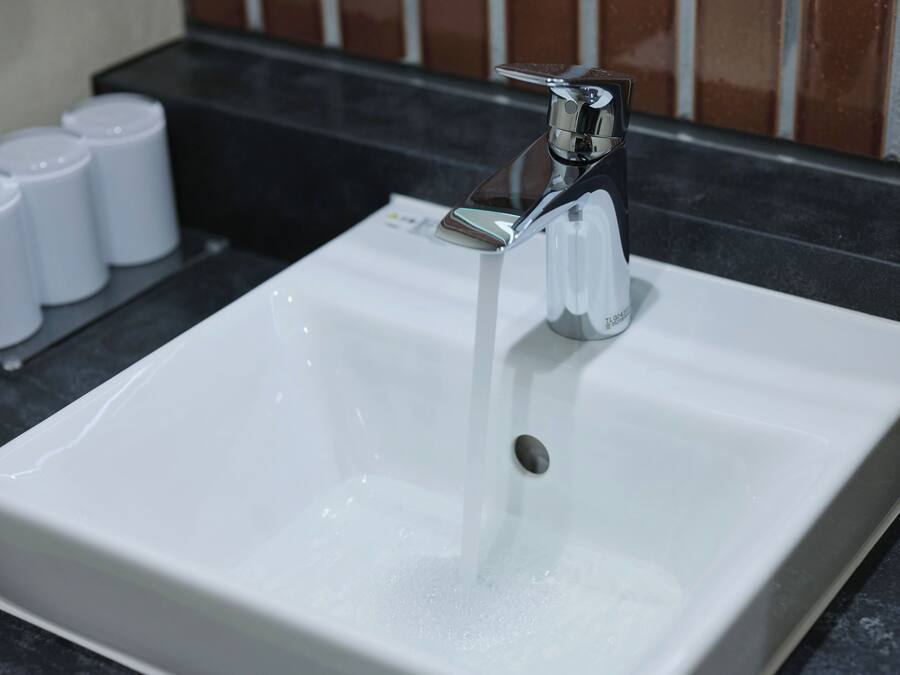 Un lavamanos blanco con grifo cromado y agua corriendo.