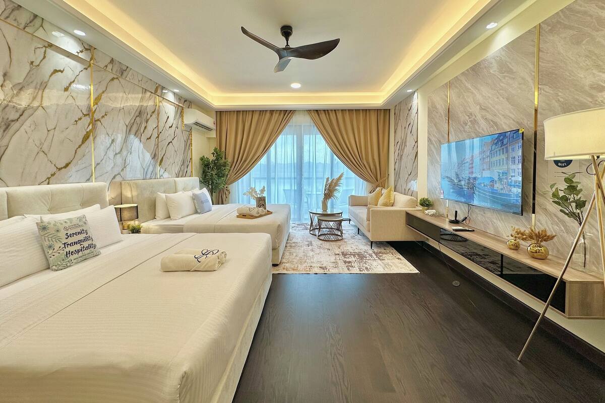 A modern hotel room with a large bed, a sofa, a TV, and a ceiling fan.