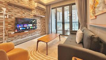 Un salon moderne avec un téléviseur à écran plat fixé à un mur texturé, un canapé, une table basse et une vue sur le balcon extérieur.