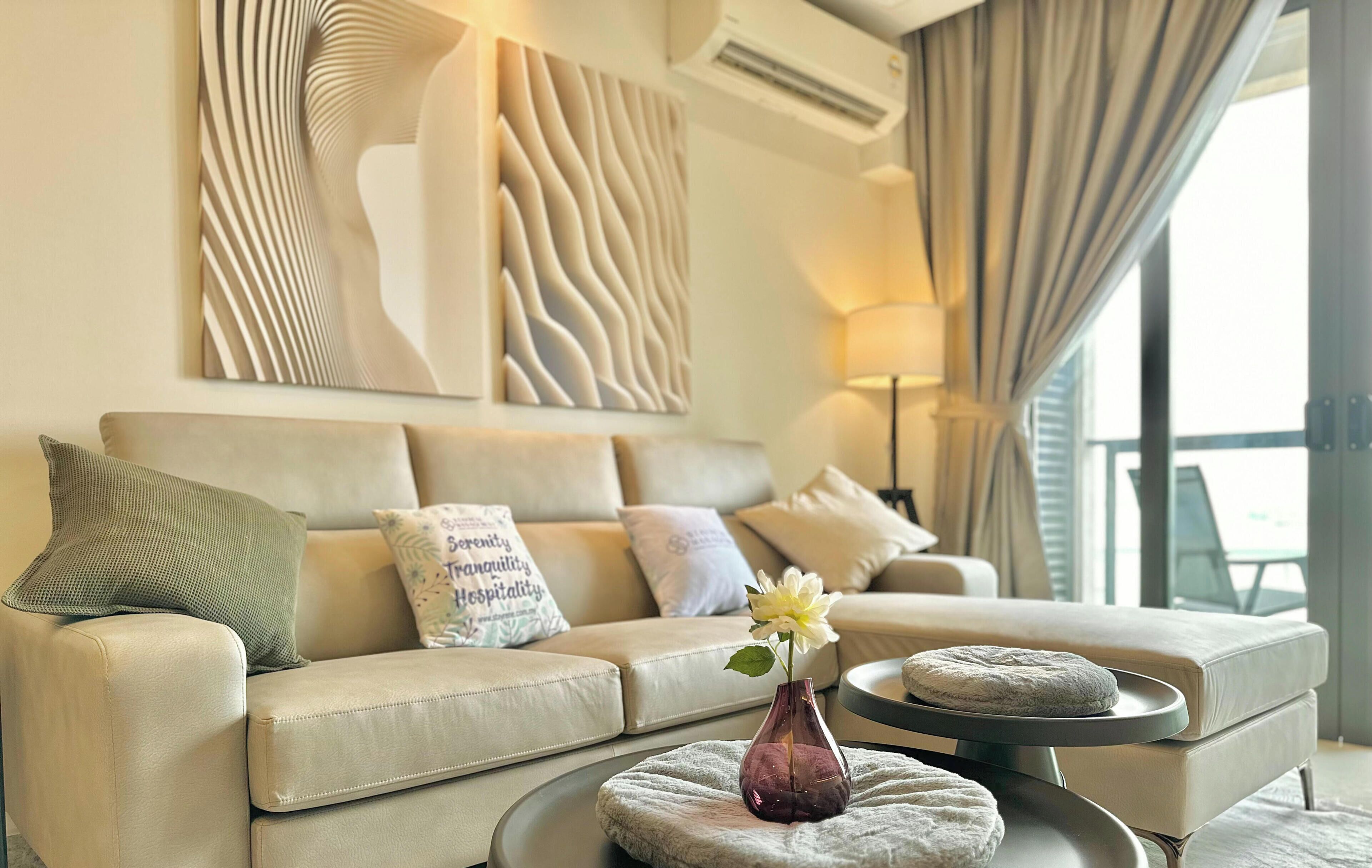 Una sala de estar moderna con un sofá color beige, almohadones decorativos, un jarrón con una flor y una mesa de centro redonda.
