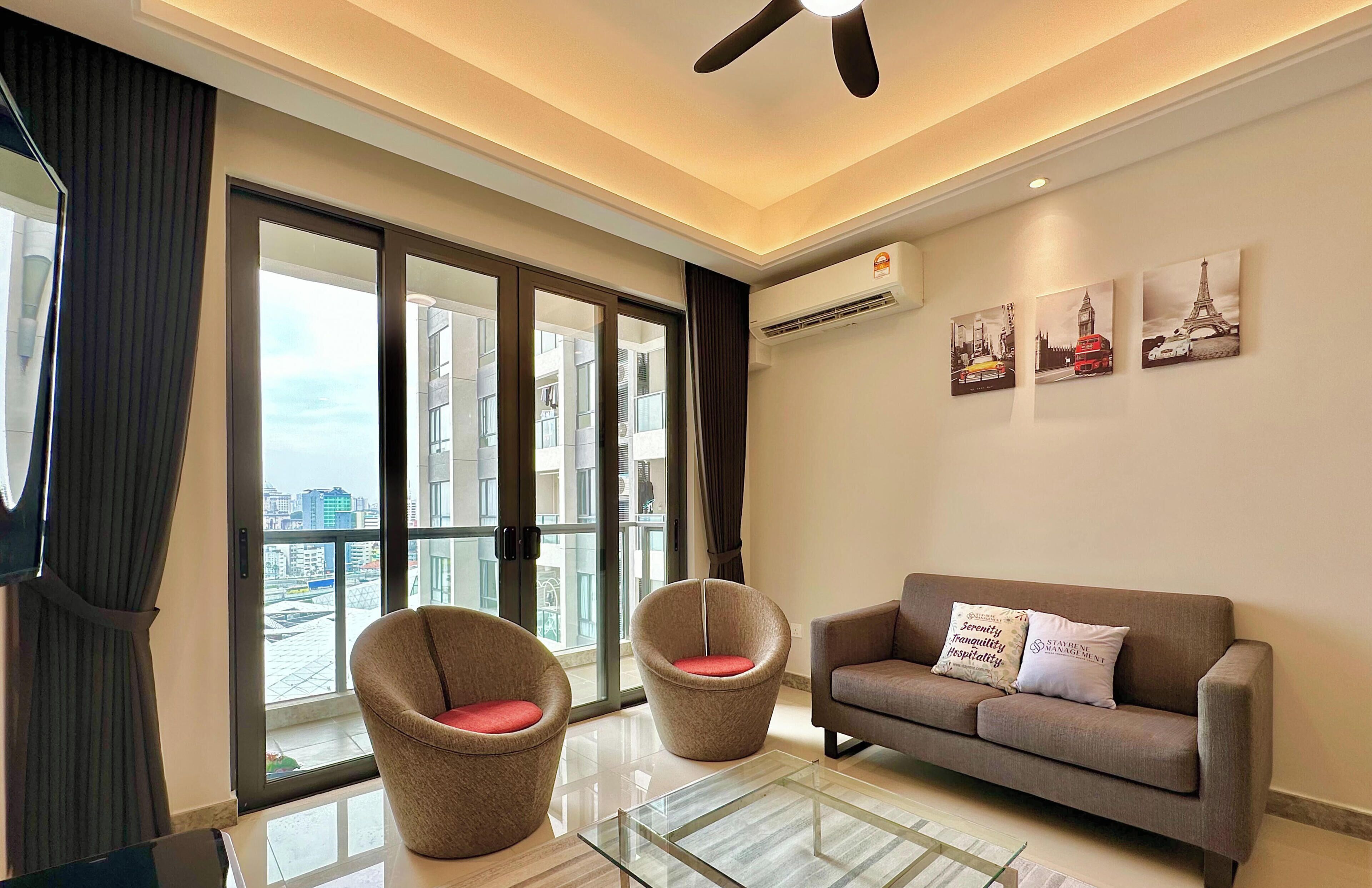 Ein modernes Wohnzimmer mit einer Couch, zwei Sesseln, einem Glastisch und einem Deckenventilator.