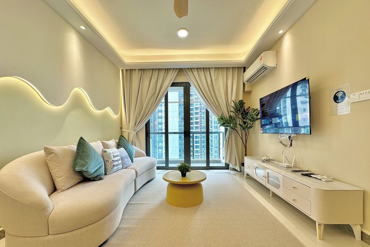 A modern living room with a curved sofa, a coffee table, a TV, and a view of high-rise buildings.
