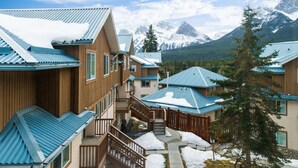 Un ensemble de cabanes en bois aux toits bleus, se dressant sur un fond de montagnes enneigées.
