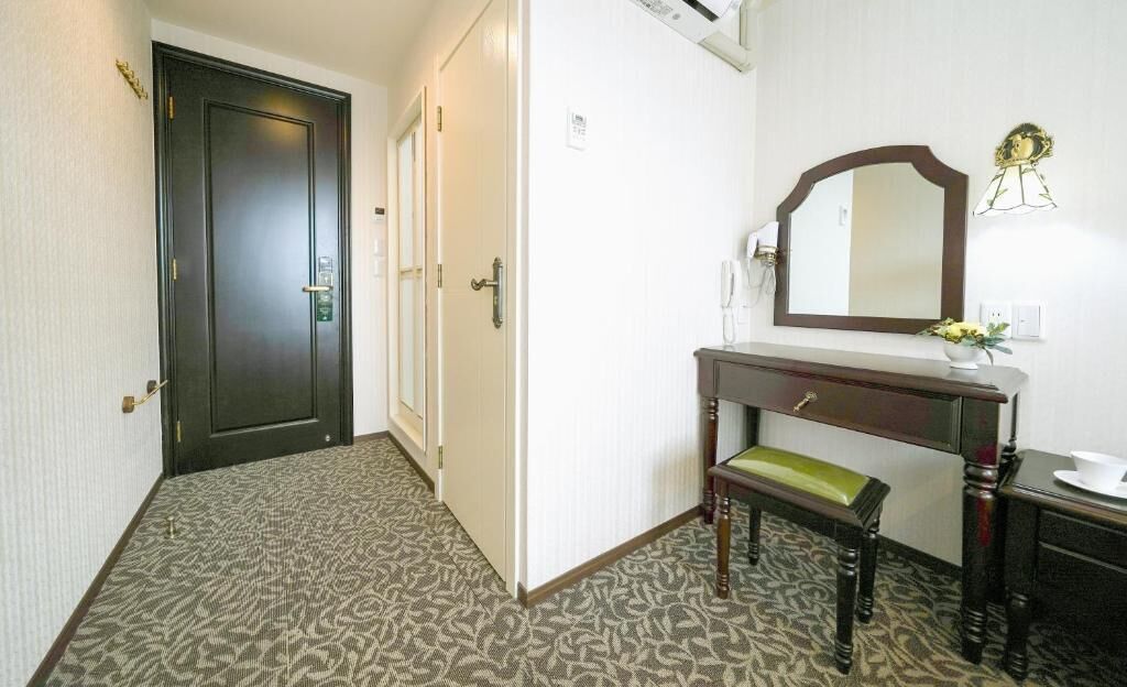 Une chambre d’hôtel avec un tapis à motifs, un banc en bois, une coiffeuse avec un miroir et une porte dotée d’une poignée.