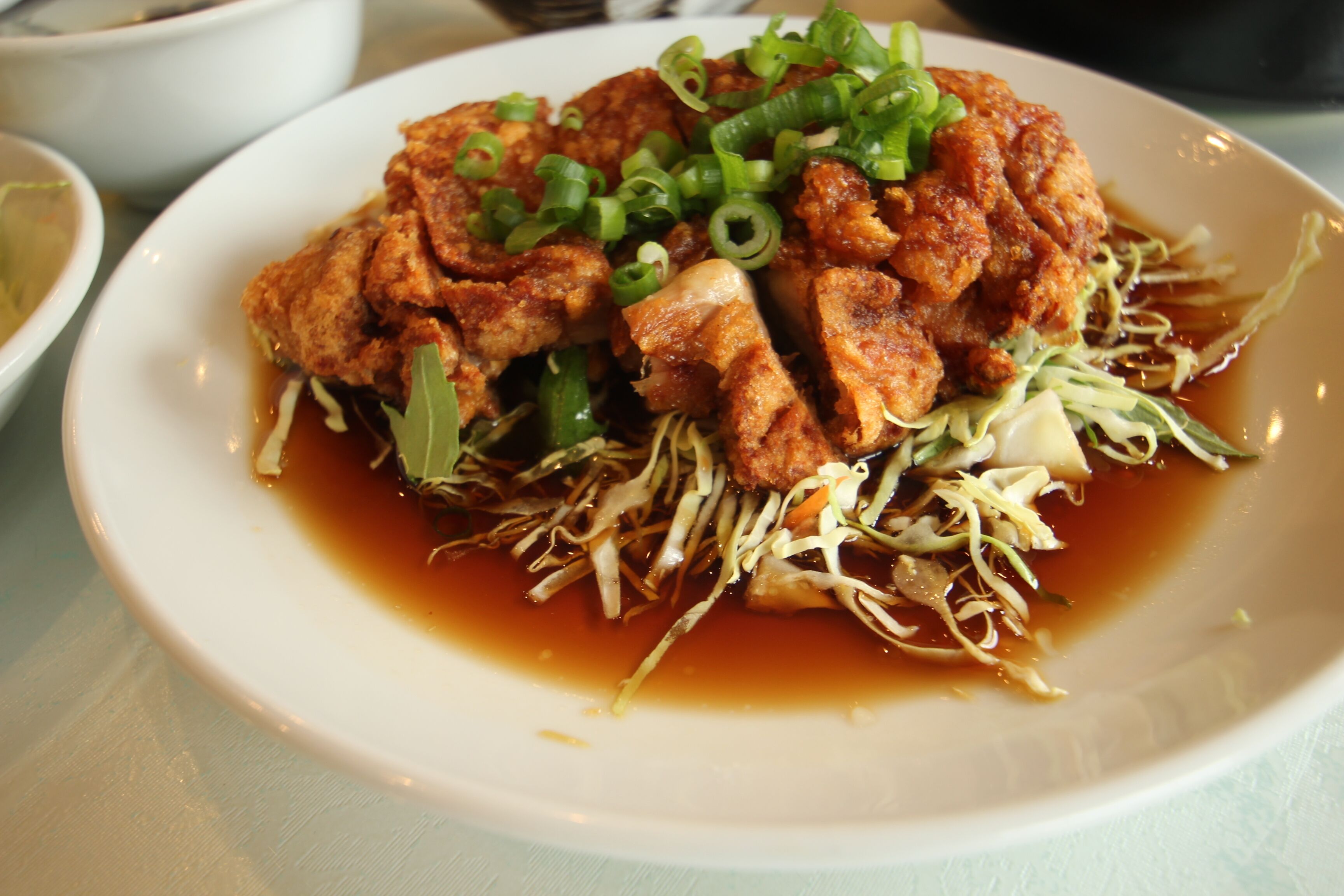 Une assiette de nourriture contenant du tofu et des oignons verts, le tout présenté sur une assiette blanche.