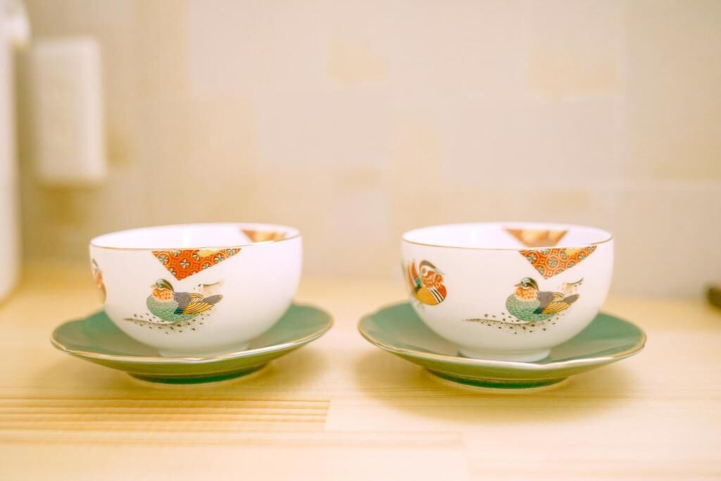 Two white cups with colorful bird designs on a green saucer, placed on a wooden surface.