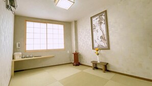 Une pièce dotée d’une grande fenêtre, d’un banc en bois, d’une petite table sur laquelle est posé un vase, et d’une œuvre d’art japonaise traditionnelle accrochée au mur.