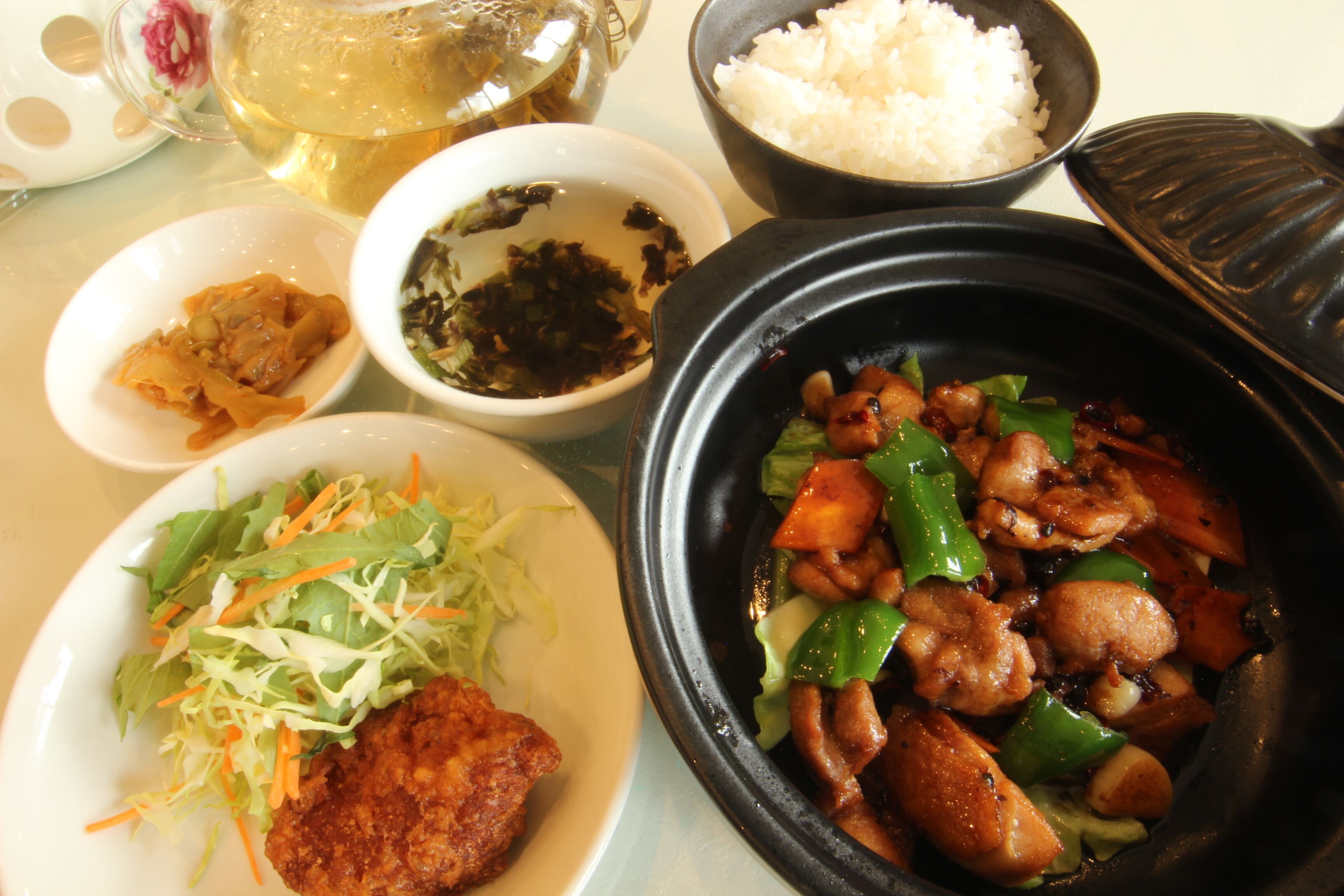 A table with various dishes including a bowl of stir-fried meat, a plate of salad, a bowl of rice, and a cup of tea.