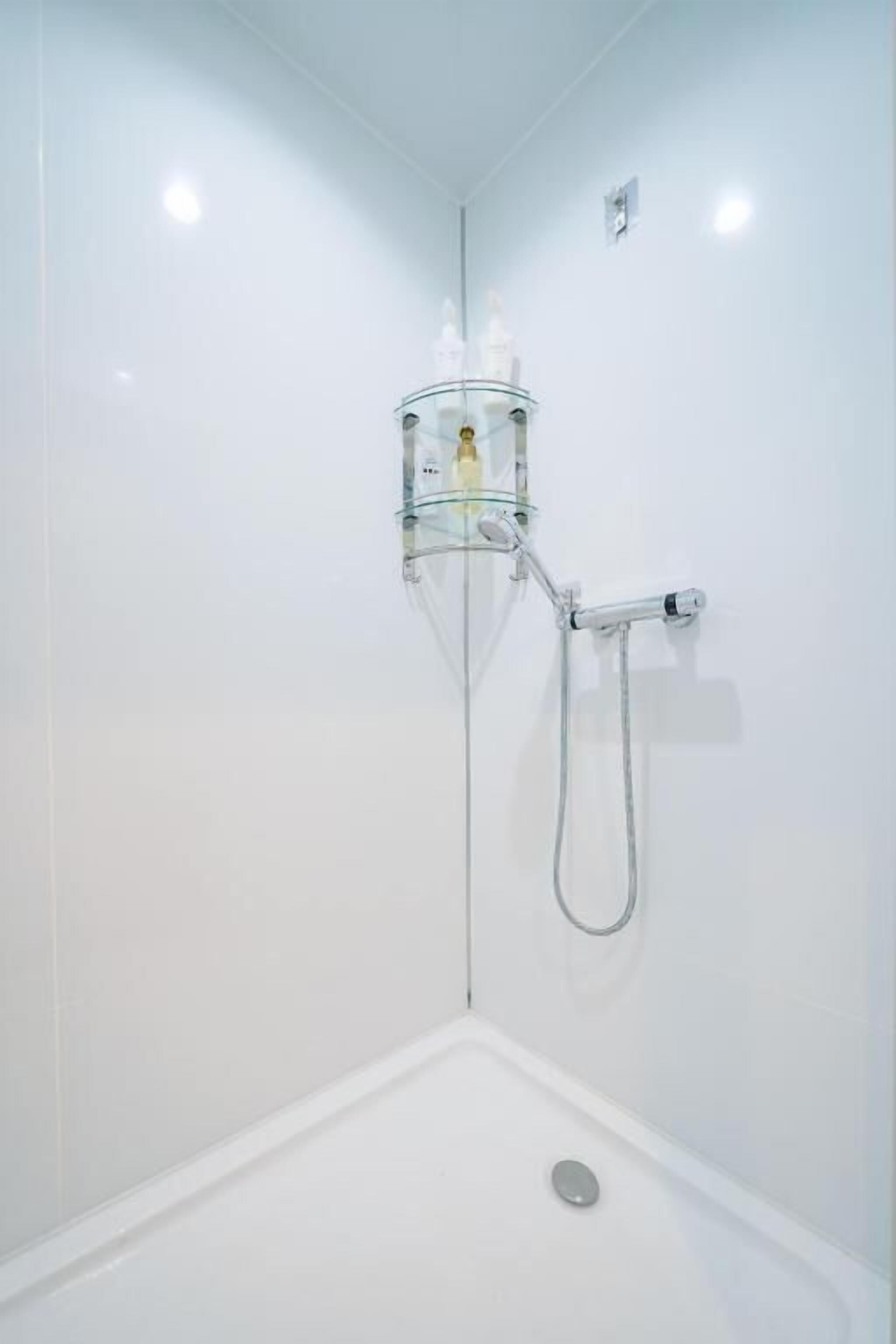 Una ducha con mampara de vidrio, cabezal de ducha de mano y panel de control en la pared.
