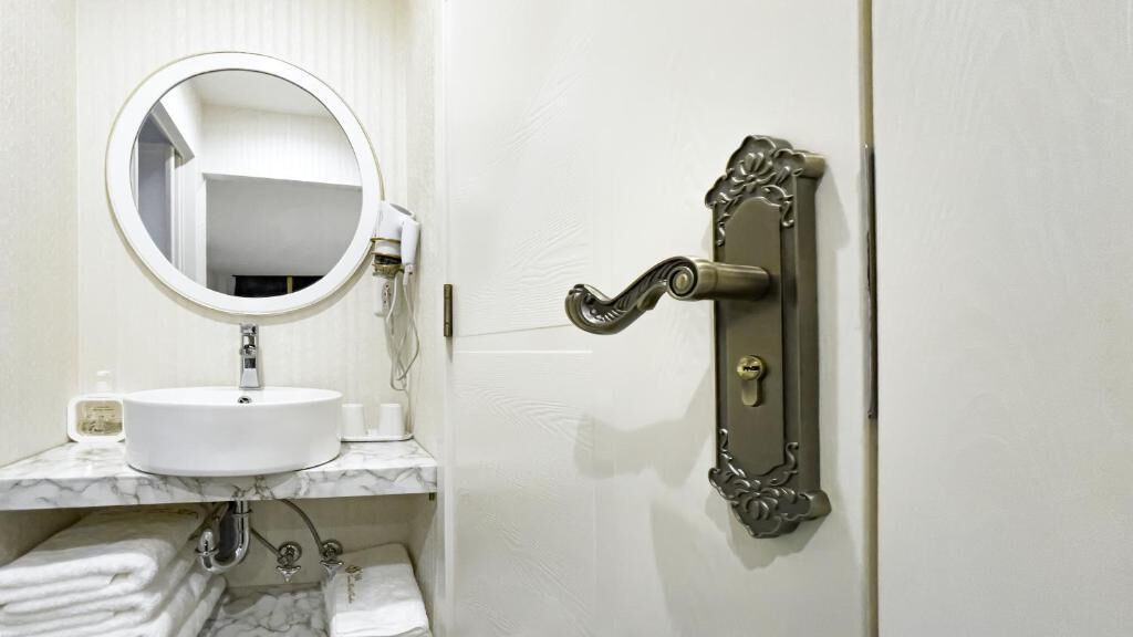 Een badkamer met een witte wastafel, een ronde spiegel en een handdoekhouder.