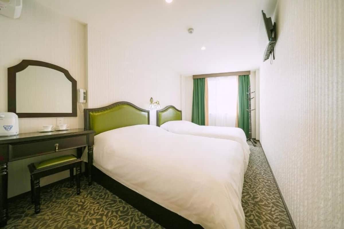 Habitación de hotel con dos camas, un escritorio con espejo, un teléfono y una ventana con cortinas.