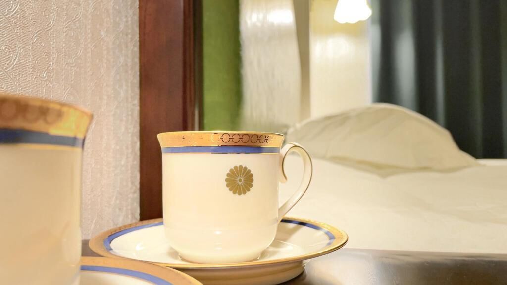 A cup and saucer on a table with a bed in the background.