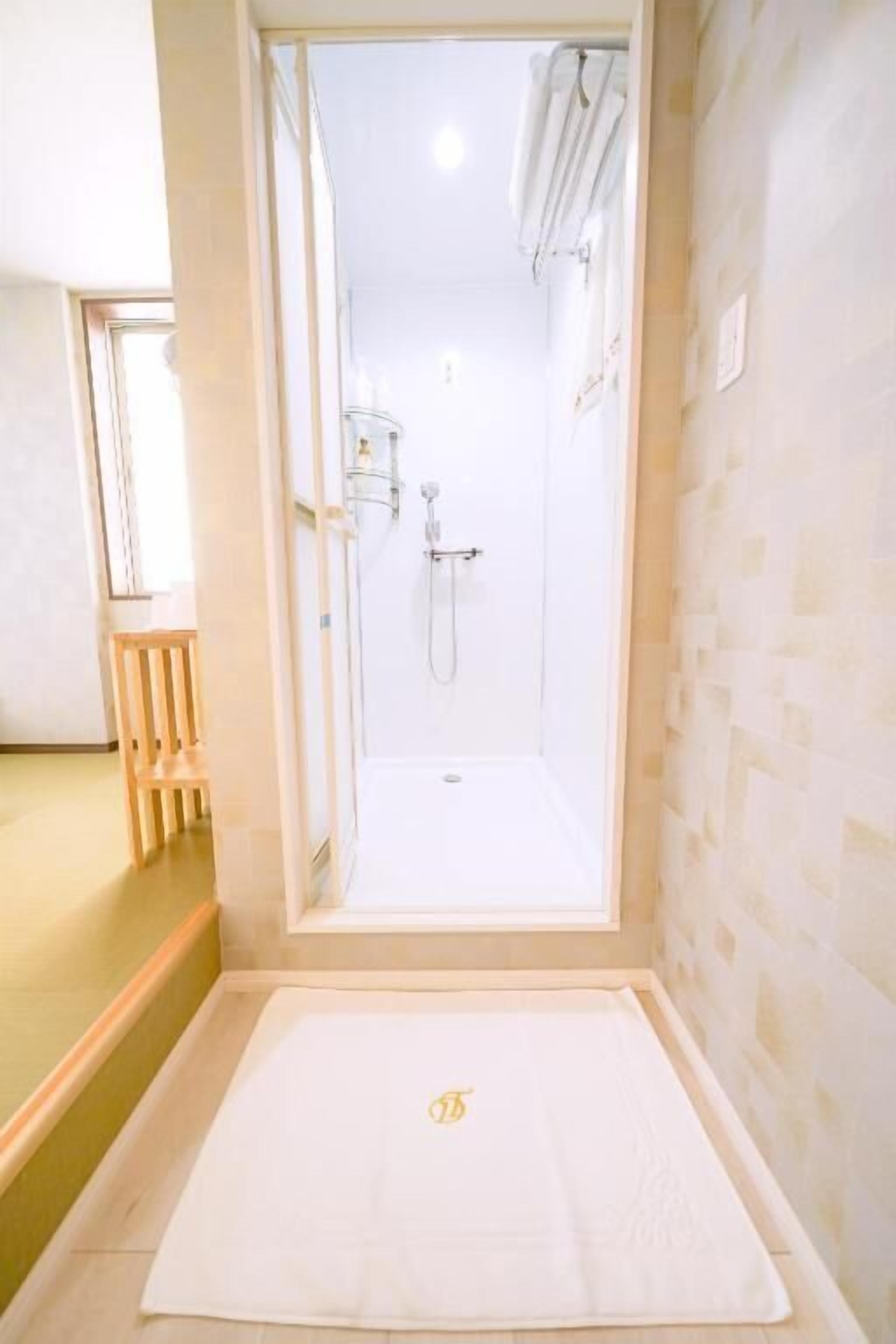 A bathroom with a shower, a wooden chair, and a towel on the floor.