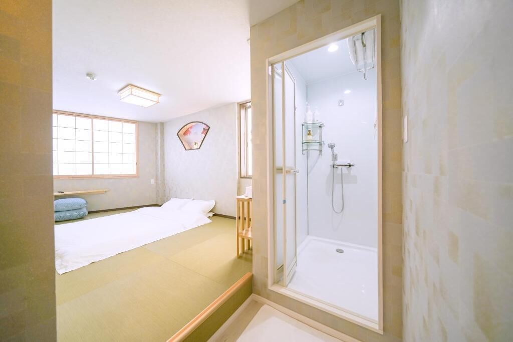 A hotel room with a large window, a bed, a shower area, and a small table.
