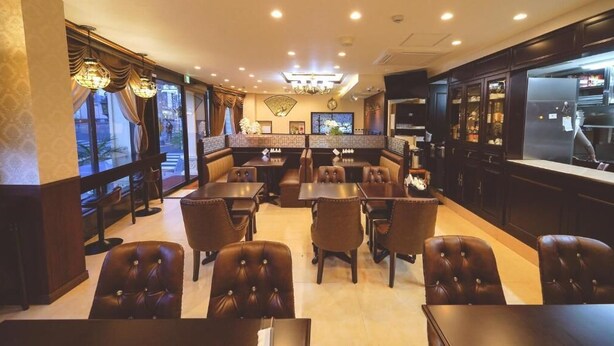 Un restaurant avec des banquettes et des tables, un coin bar et une cuisine visible à travers une paroi en verre.