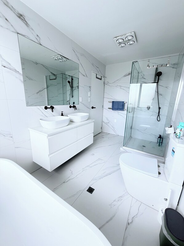 A modern bathroom with a white vanity, a large mirror, a glass-enclosed shower, and a white bathtub.