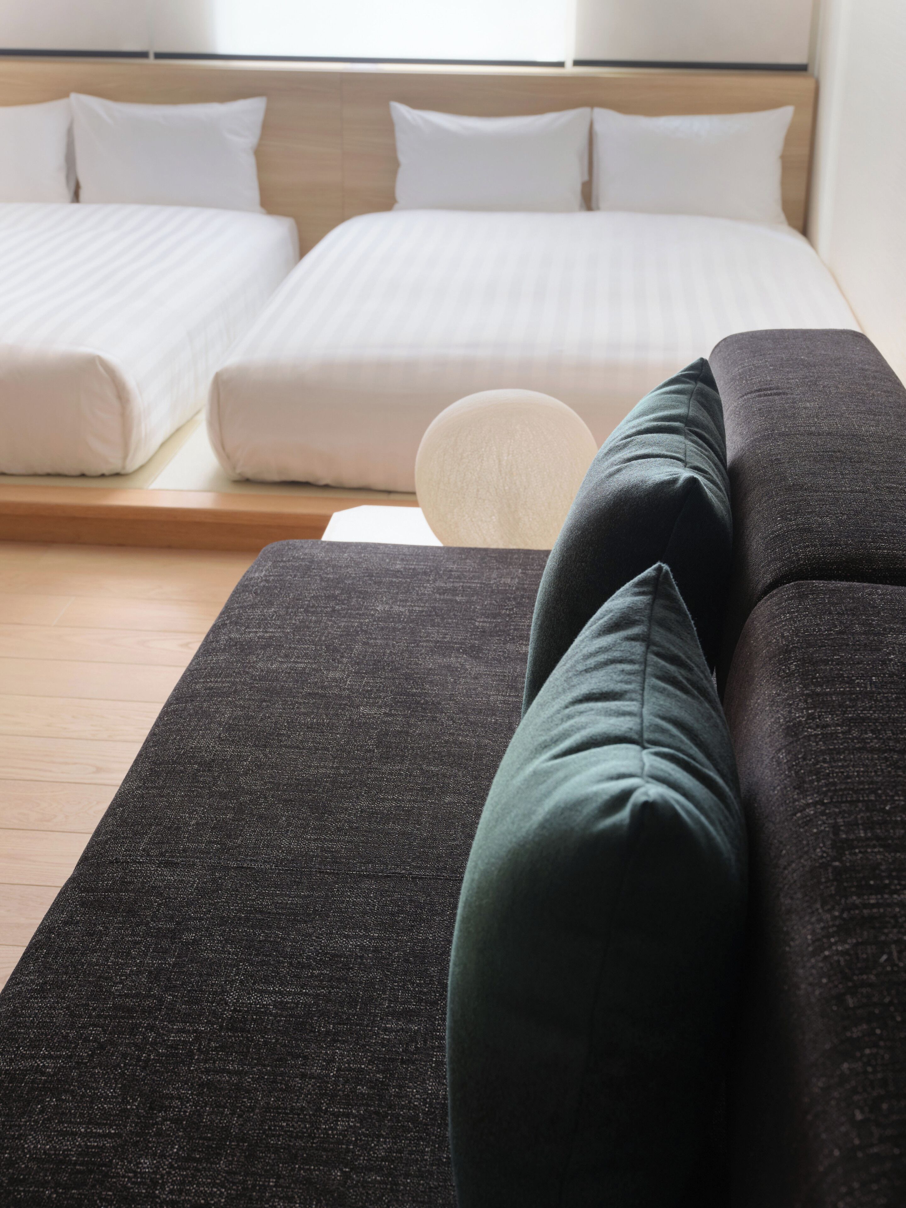 Une chambre d’hôtel avec un lit, deux oreillers, un canapé et un objet rond blanc posé sur le sol.