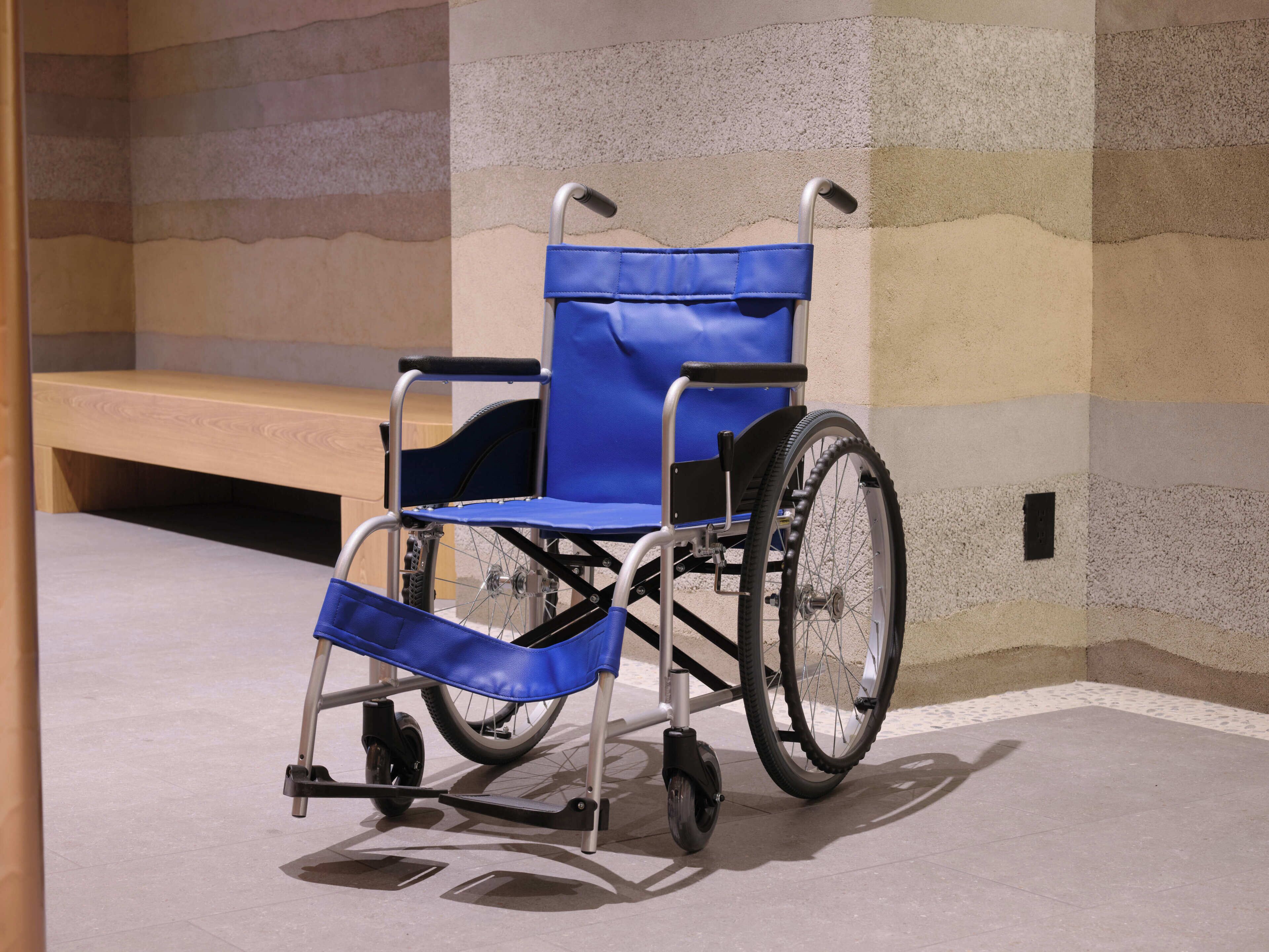 Una silla de ruedas en una habitación con un banco y una pared con textura.