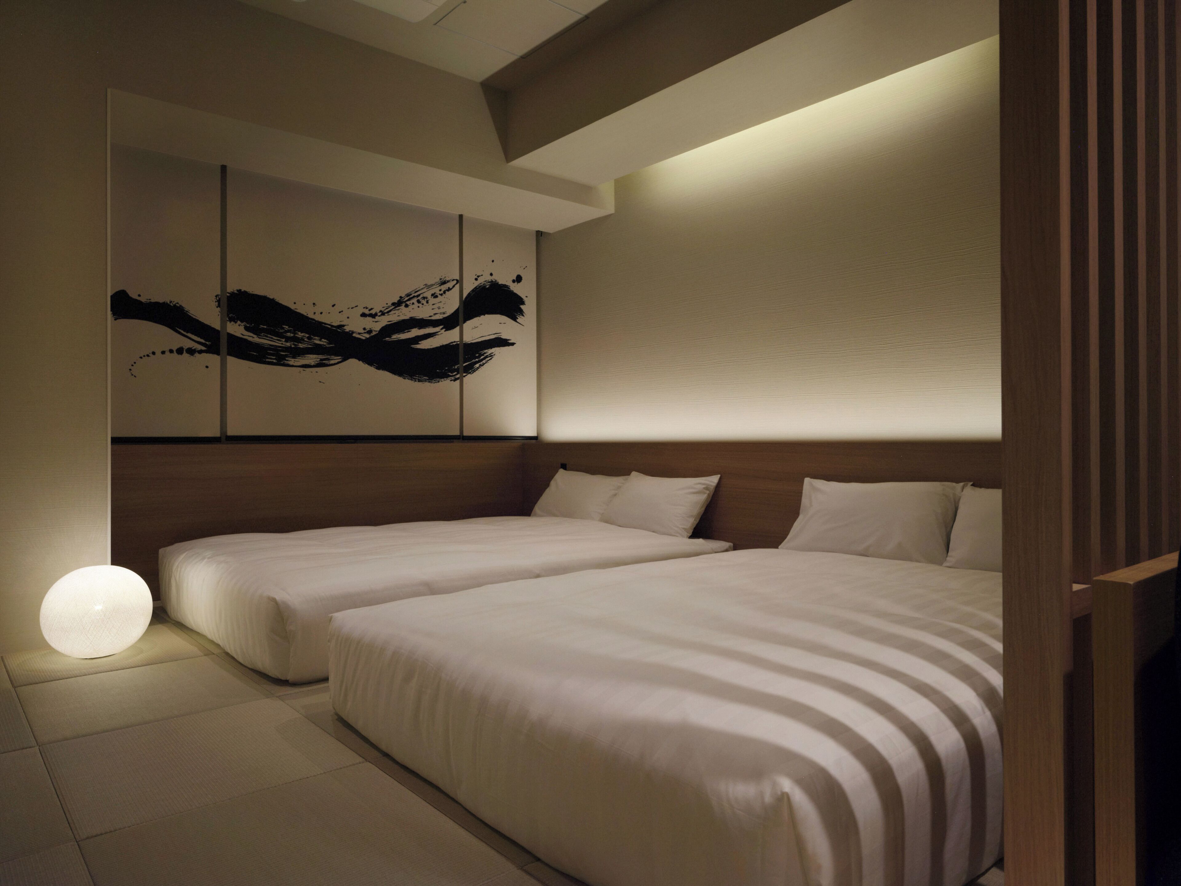A hotel room with two beds, a large wall art piece, and a round light fixture.