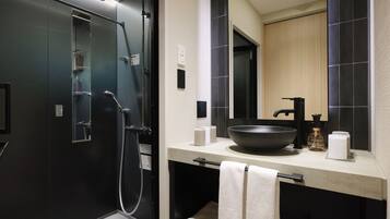 A modern bathroom with a large mirror, a black sink, and a walk-in shower.