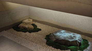 A corner of a room with a pebble-lined floor, two rocks with moss, and a textured wall.
