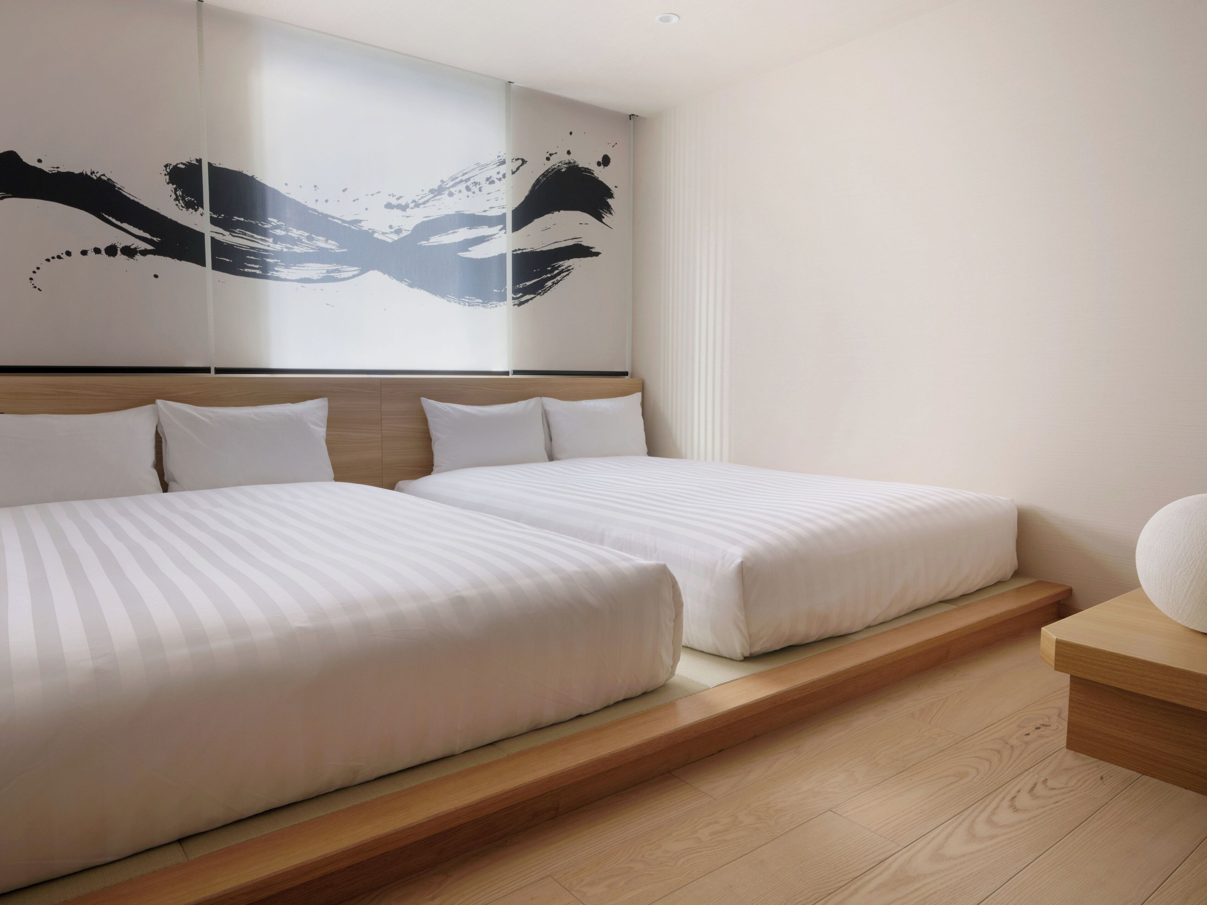 Una habitación de hotel moderna con dos camas, un cabecero de madera, un cuadro abstracto grande y una mesita de noche pequeña.