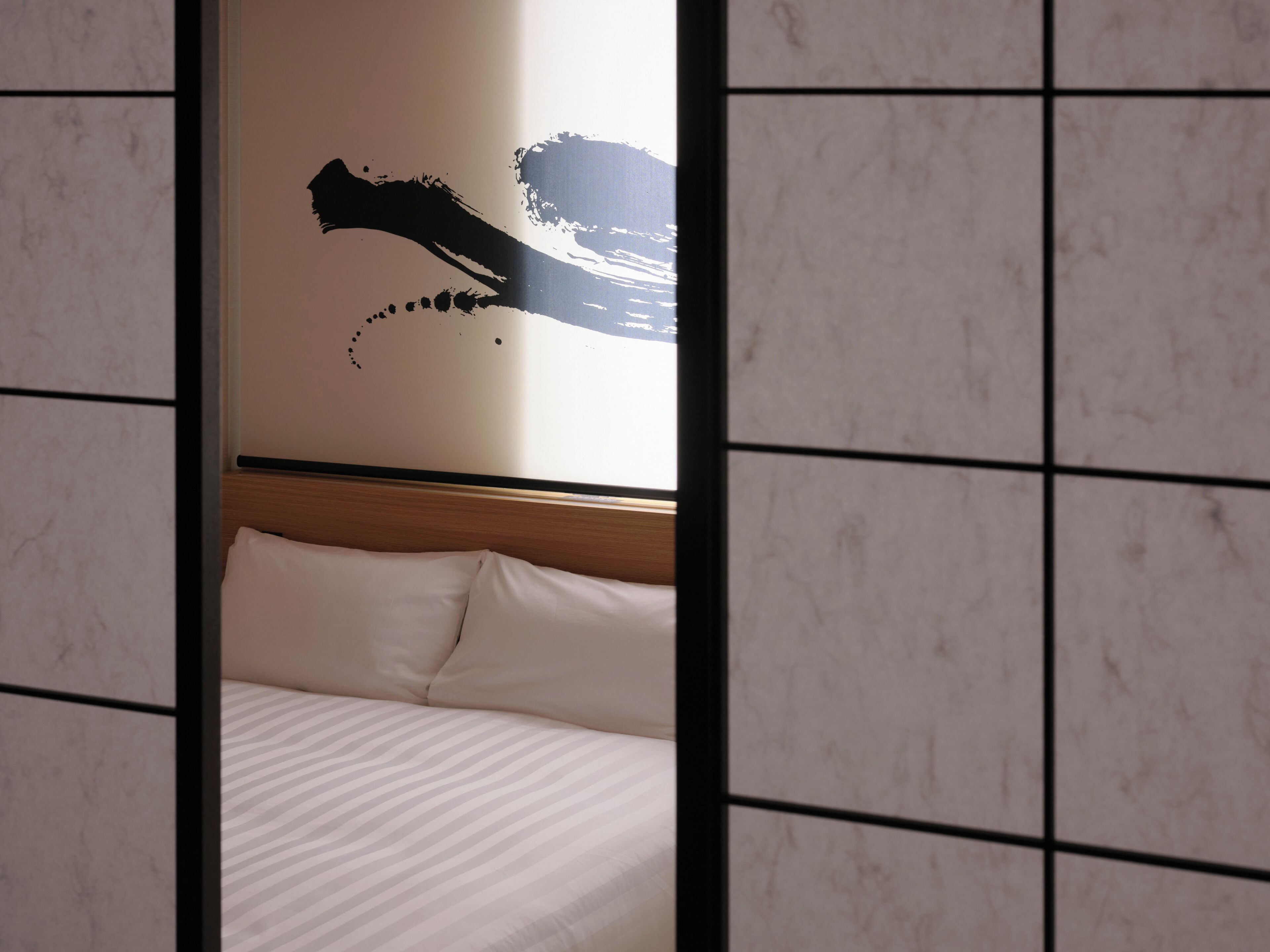 A hotel room with a bed, a headboard, and a wall with a black abstract design.