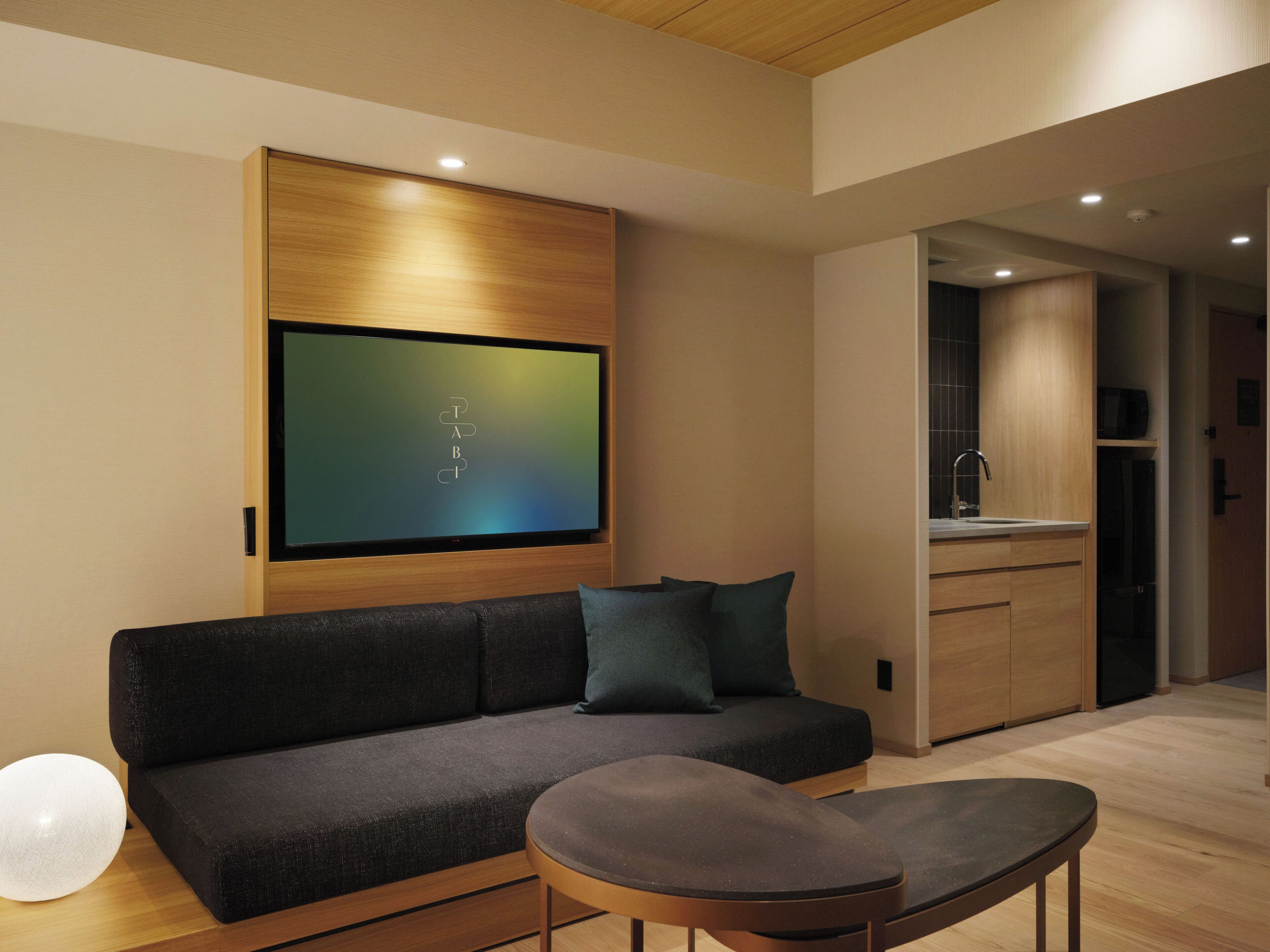 A modern living room with a dark sofa, a round table, and a flat-screen TV mounted on the wall.
