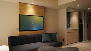 Ein modernes Wohnzimmer mit einer dunklen Couch, einem runden Tisch und einem flachbildfernseher an der Wand.