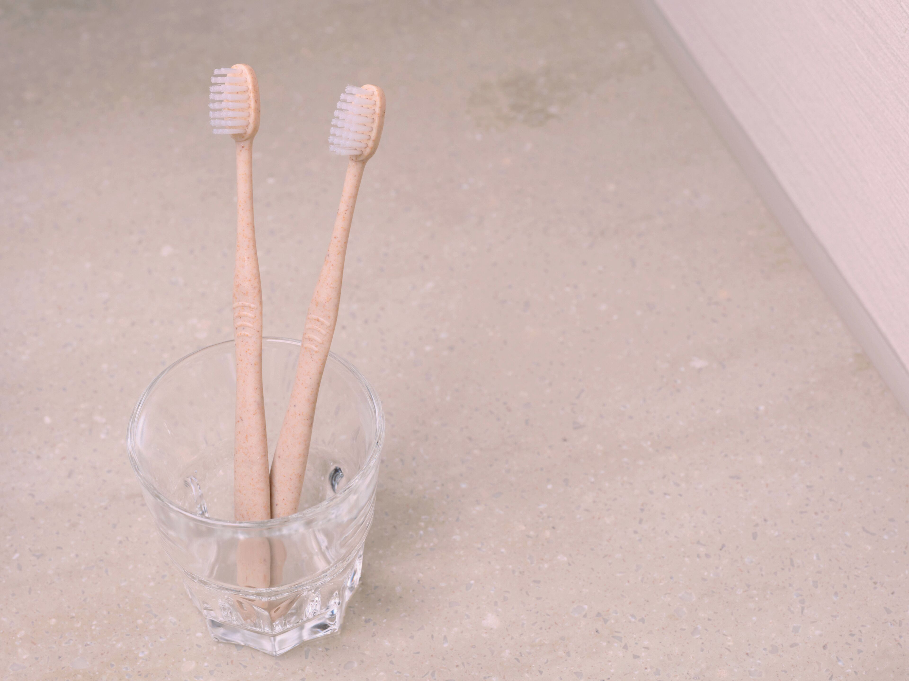 Two toothbrushes in a clear glass cup on a countertop.