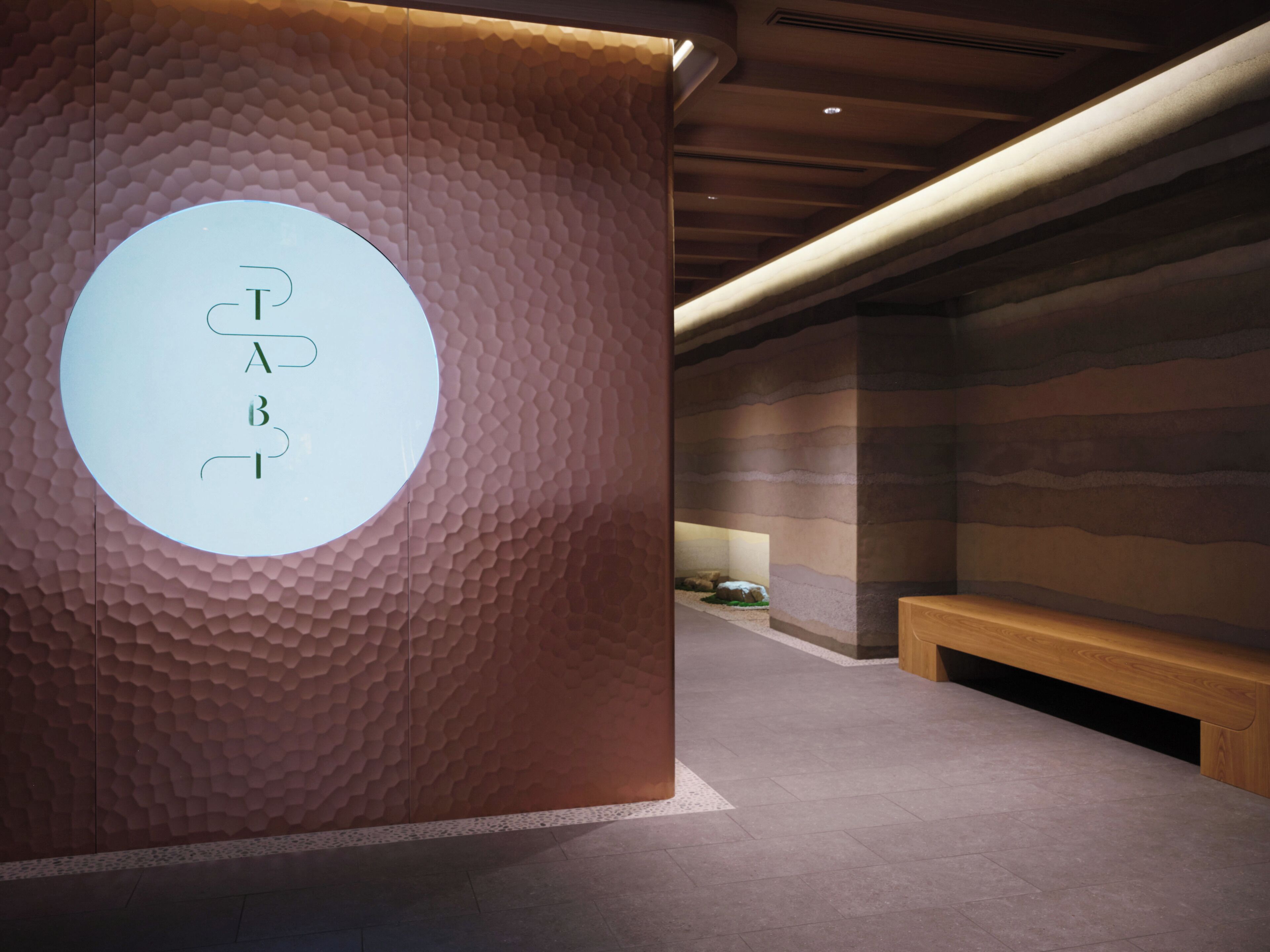 A modern interior with a textured wall, a circular sign with letters, and a wooden bench.