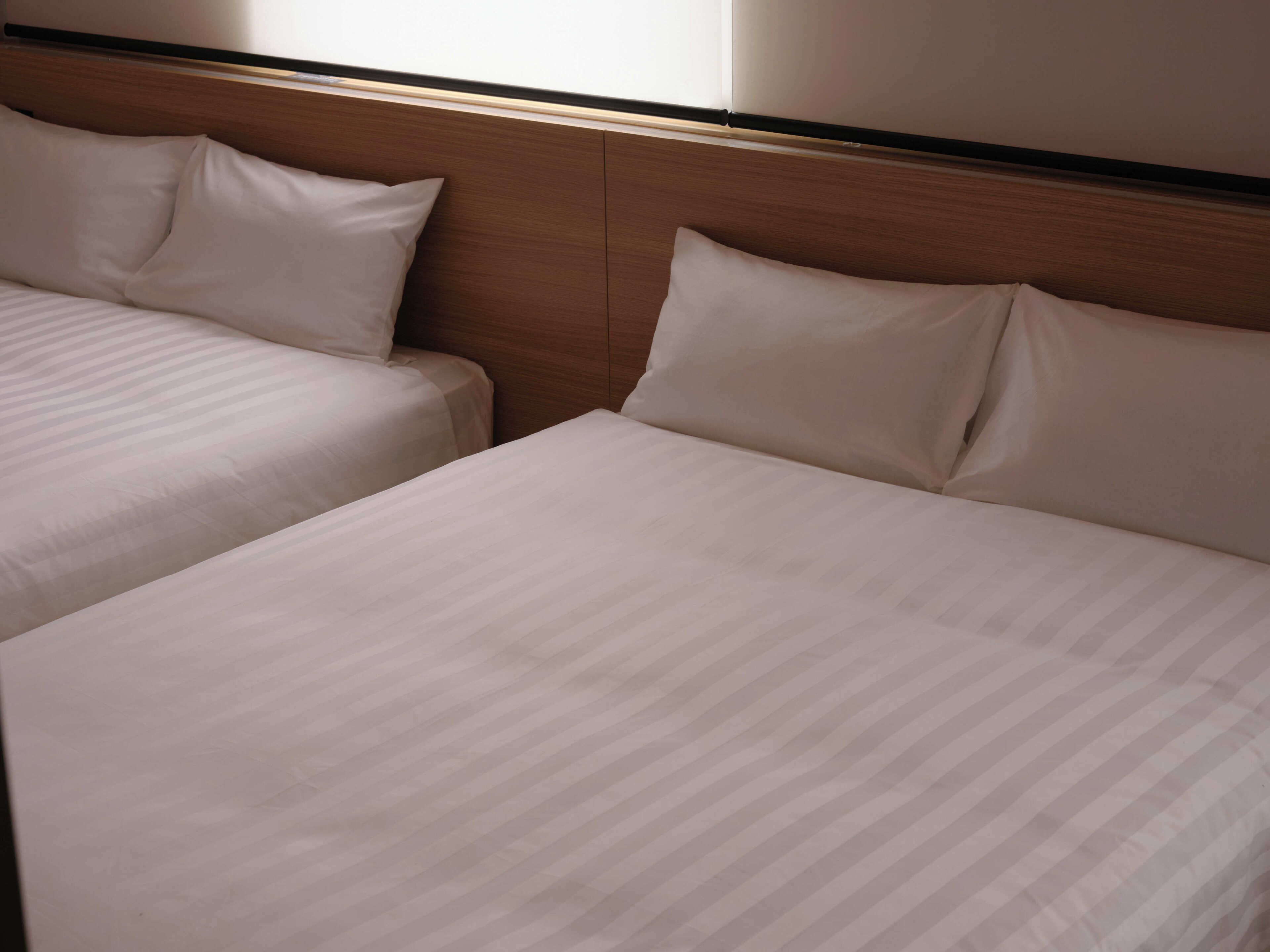 A hotel room with two beds, wooden headboard, and a window.