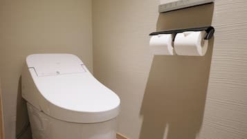 A toilet with a control panel, a toilet paper holder on the wall, and a textured wall.