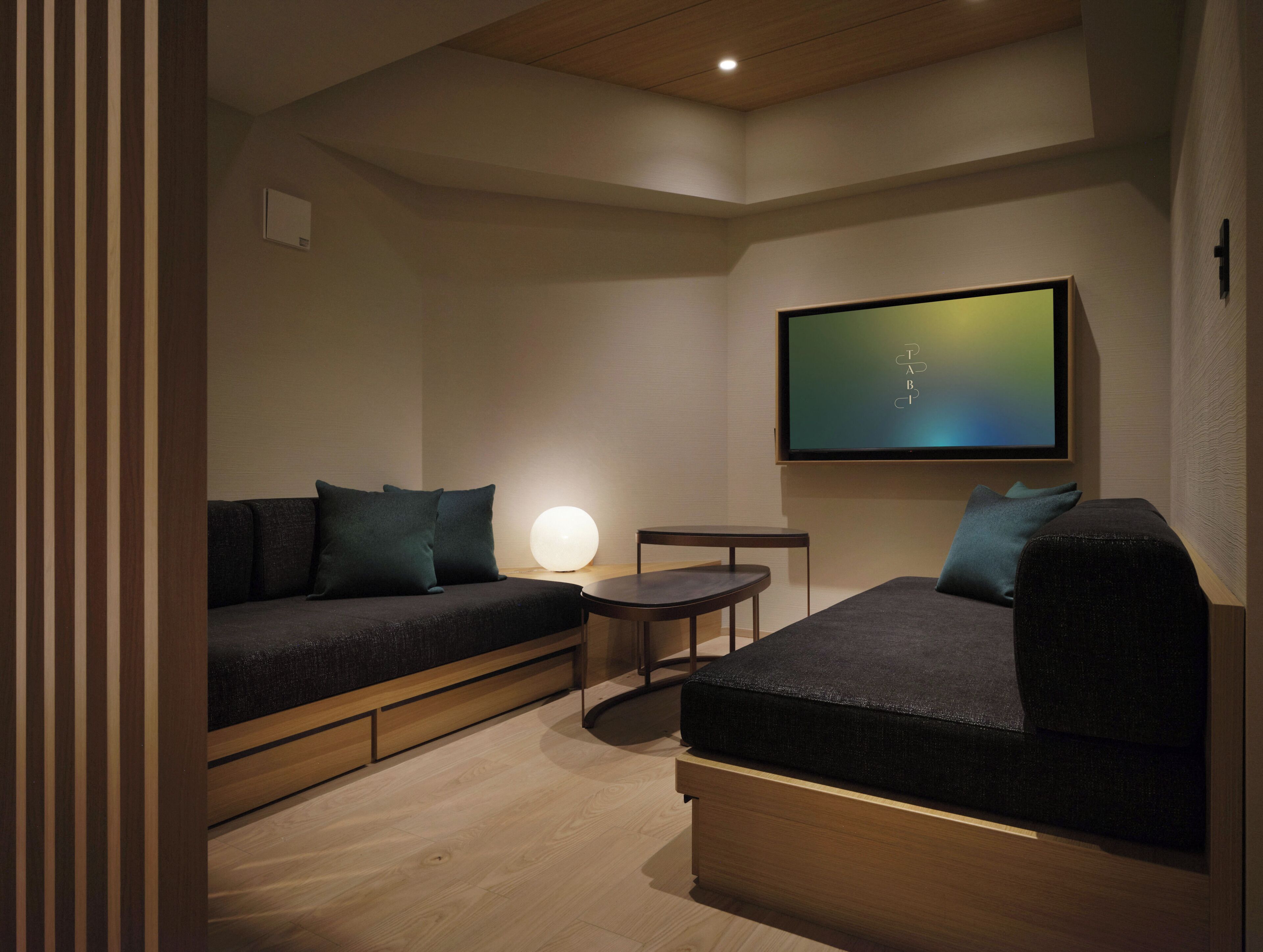 A modern living room with a sofa, a small table, a lamp, and a flat-screen TV mounted on the wall.