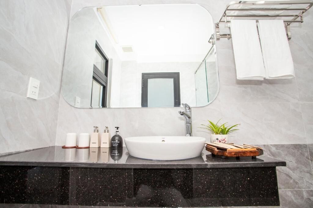 A bathroom with a large mirror, a white sink, and a vanity with toiletries.