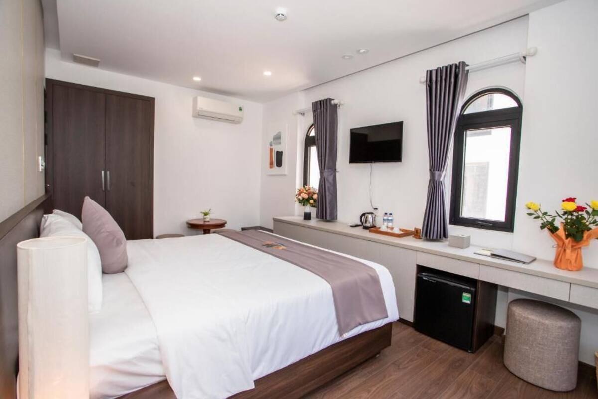 A modern hotel room with a large bed, a desk, a television, and a wardrobe.