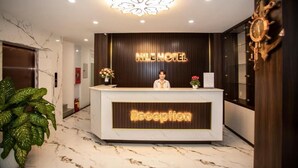 A hotel reception desk with a marble floor, a receptionist, and a clock on the wall. - Nile Hotel Phu Yen  (Tuy Hoa)