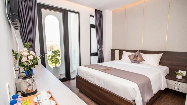 A modern hotel room with a large bed, a bedside table with a tray, a coffee maker, and a view of the outdoors. - Nile Hotel Phu Yen  (Tuy Hoa)