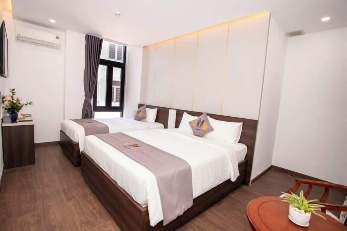 A hotel room with two beds, a small table, a potted plant, and a window with curtains.