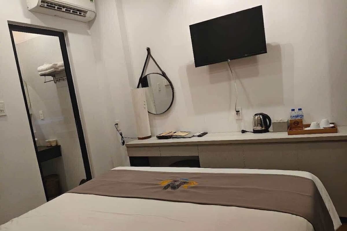 A hotel room with a bed, a desk with a flat-screen TV, a mirror, and a small table with toiletries.