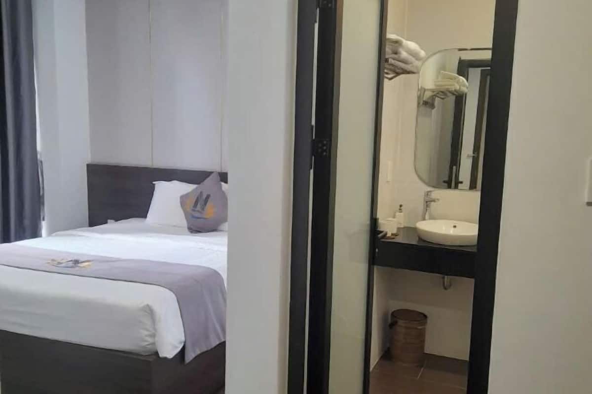 A hotel room with a bed, a bedside table, a mirror, and a bathroom with a sink and toilet.