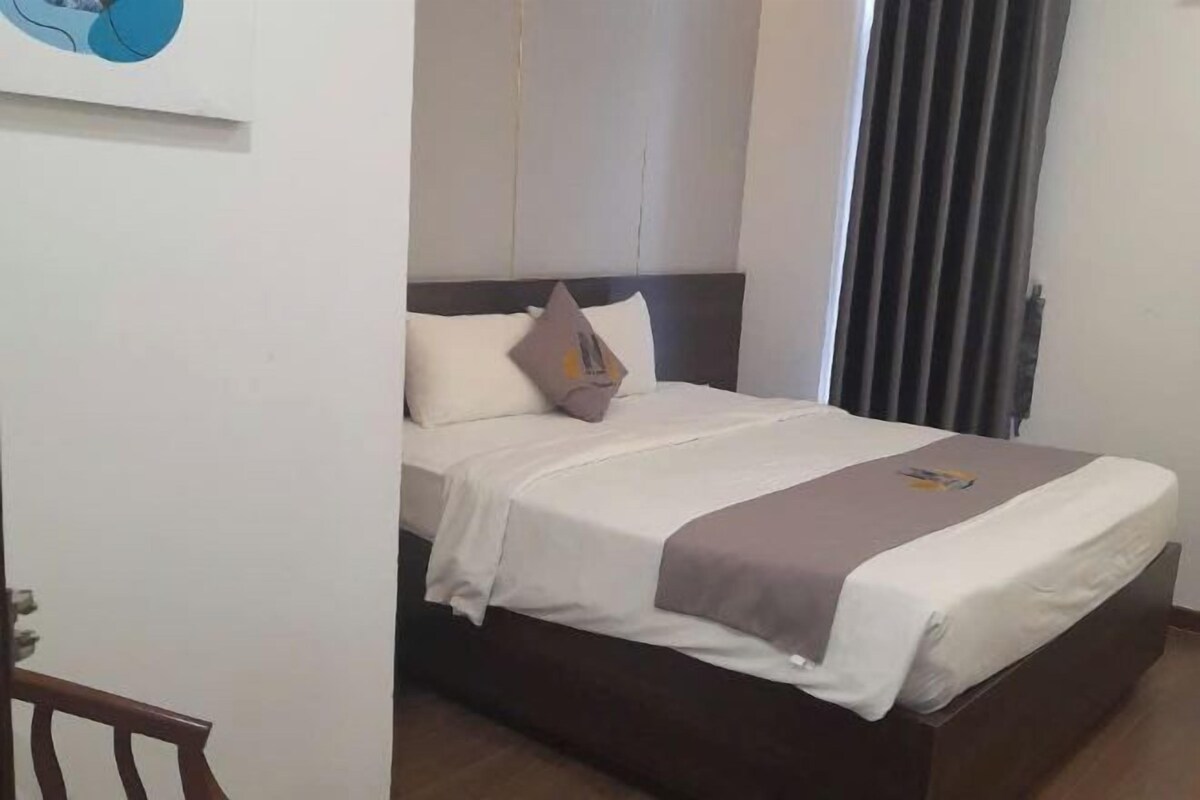 Ein Hotelzimmer mit Bett, Kopfstütze, einem Fenster mit Vorhängen und einer Tür.