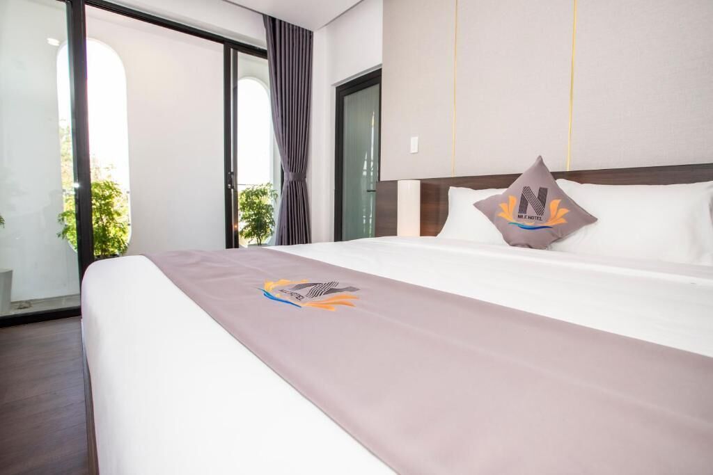 A hotel room with a large bed, a view through a sliding glass door, and a pillow with the hotel's logo.