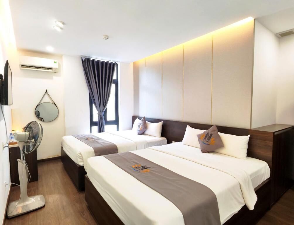 A hotel room with two beds, a flat-screen TV, an air conditioner, a fan, and a window with curtains.
