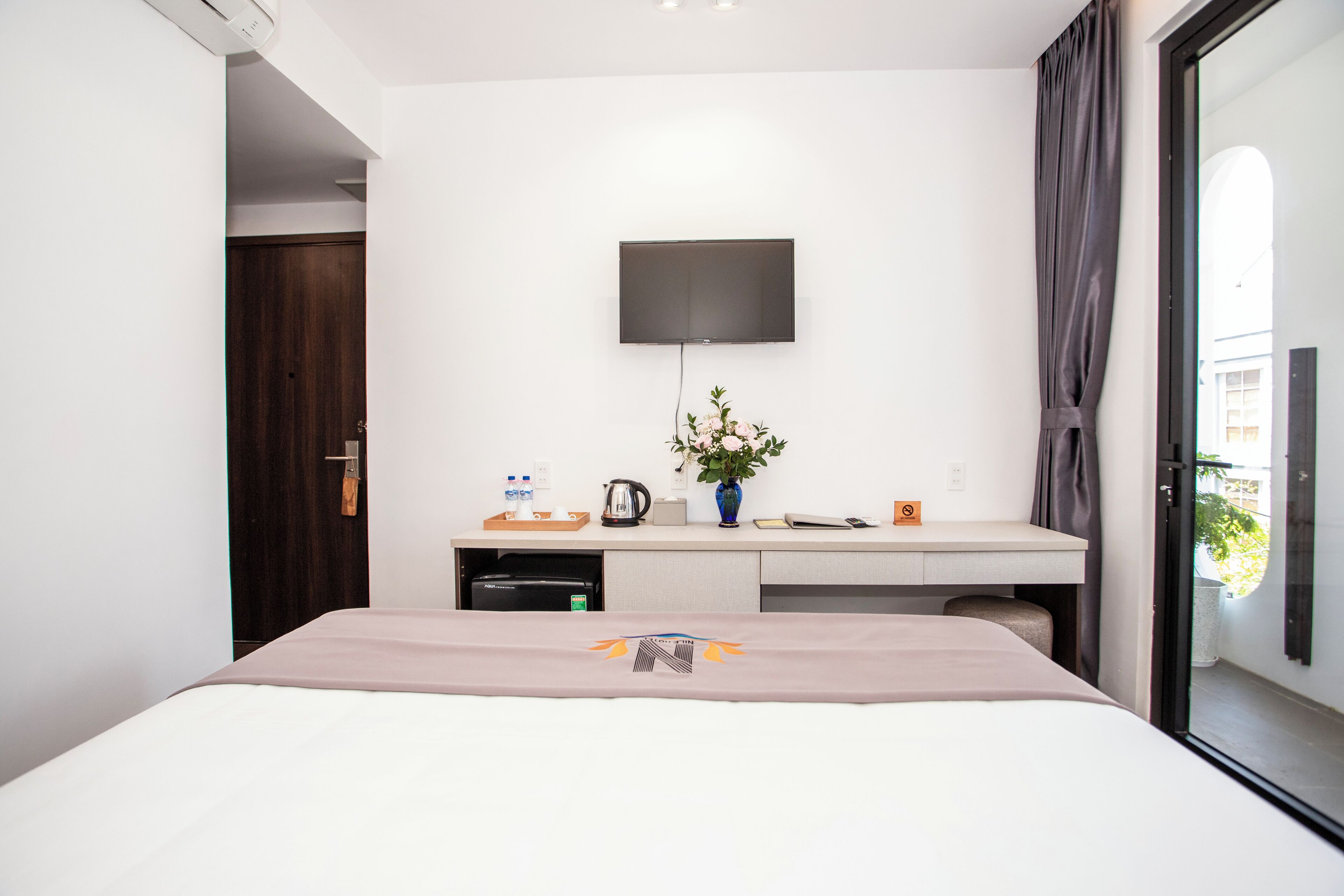 Ein modernes Hotelzimmer mit Bett, Schreibtisch, Flachbildfernseher, Pflanze und einem Fenster mit Vorhängen.