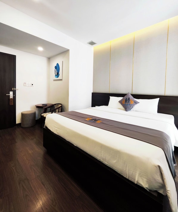 Una habitación de hotel moderna con una cama grande, una mesita de noche, una silla y una pequeña mesa redonda.