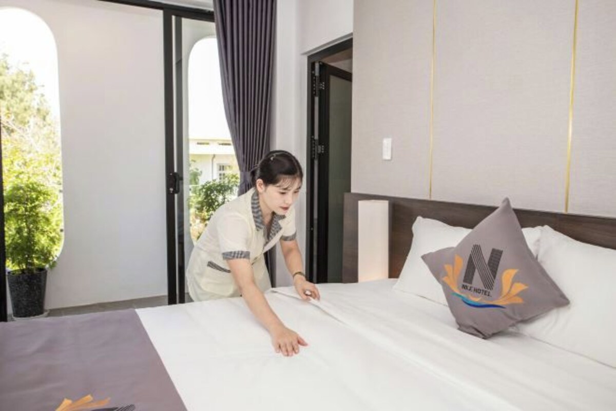 A hotel room with a neatly made bed, a pillow with a logo, and a view of the outdoors.