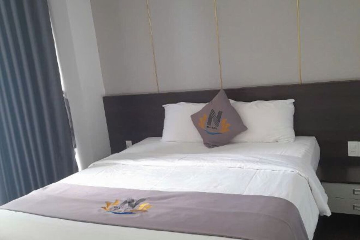 A hotel room with a bed, a pillow, a bedside table, and a window with curtains.